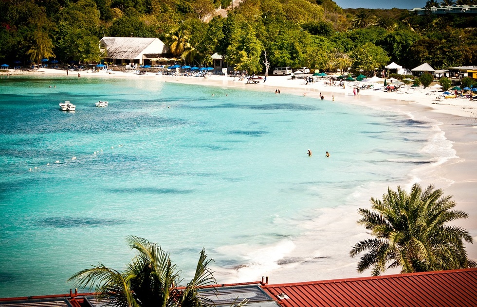 People swimming, sitting in lounge chairs, and walking on Long Bay beach in Antigua.