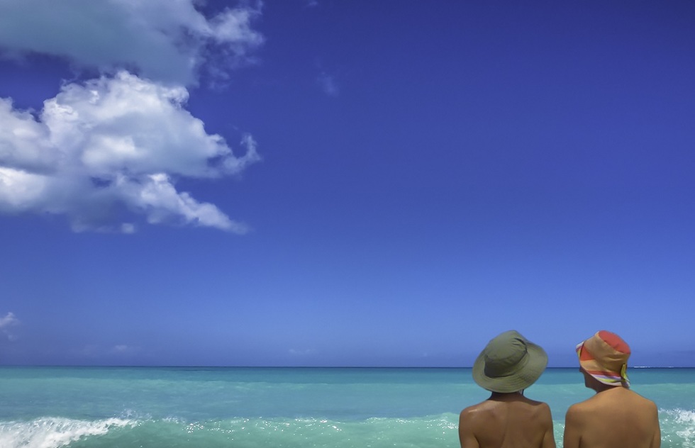 Two people in the water at Eden Beach, Antigua, a nude beach. Only their bare backs are visible.